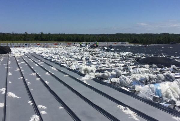 Storm damaged roof with work crew visible in background