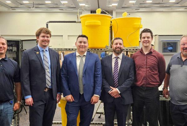 UNF Process Skid team members pose in front of their senior design project. From left are Greg Kline of Vega Americas; Daniel Fowler, 电; Adrian Hoover, 机械, 布莱斯色鬼, 机械; Lake Miller, 电; and 澳门足彩app的 Christian Beckman.